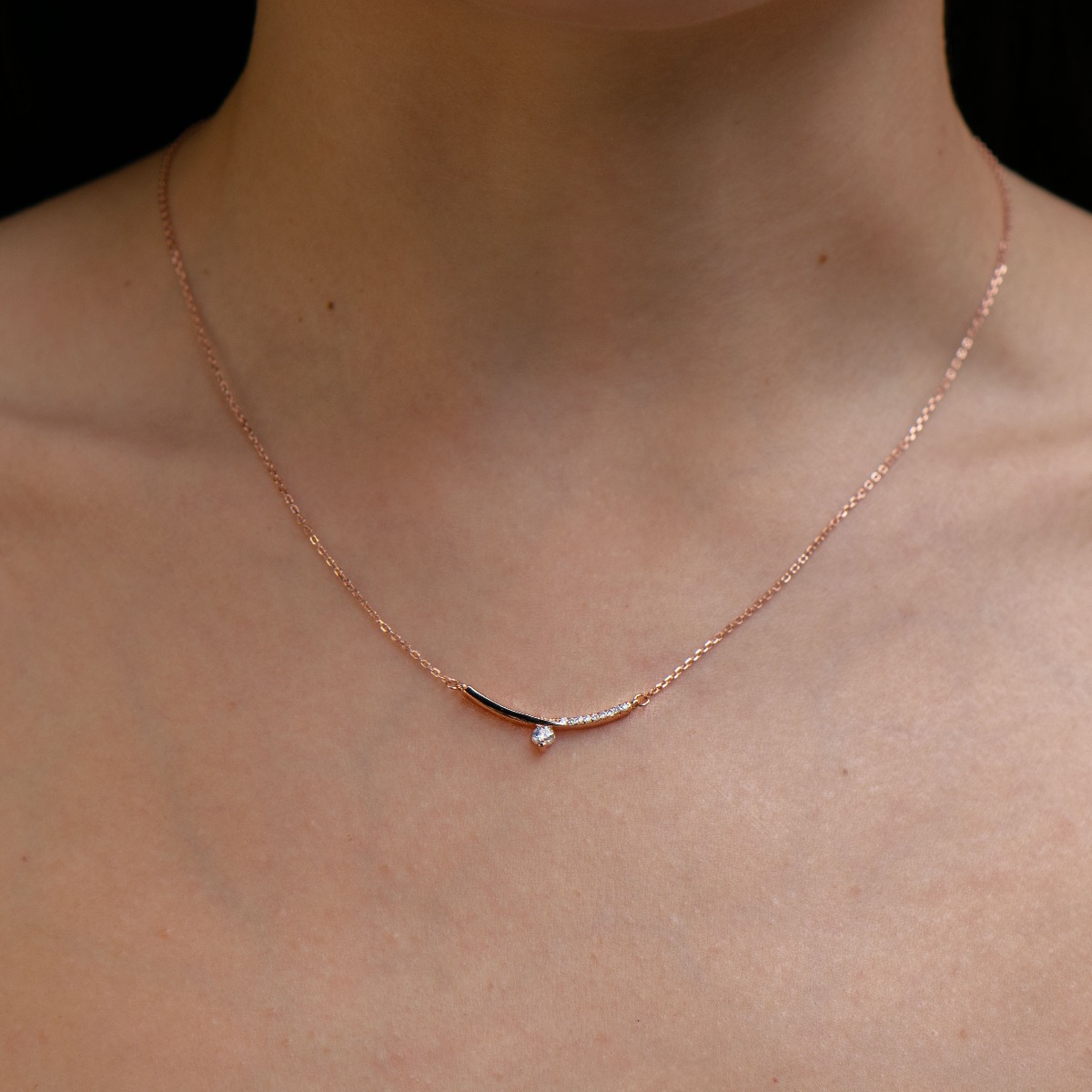 Stylish women's necklace with an exquisite design in rose silver. The piece of jewelry is charmingly crafted - a delicate chain holding a fine element, elegantly decorated with glittering zircons.