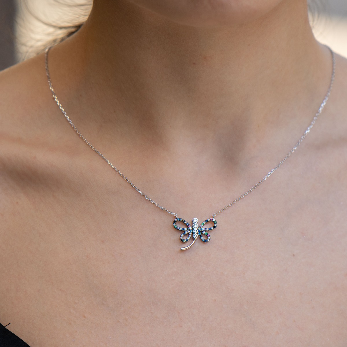 An elegant women's necklace in the shape of a dragonfly, masterfully sculpted from rhodium-plated silver and studded with delicate multi-colored zircons.