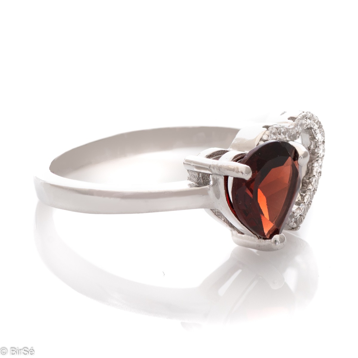 A spectacular ring made of a fine combination of rhodium-plated silver and stunning cubic zirconia stones, elegantly covering a beautiful heart. An enchanted natural garnet stone is gently nestled against the heart. The jewel is part of a set of dangling 